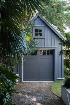 a gray garage with two windows in the front and one door on the side, surrounded by palm trees