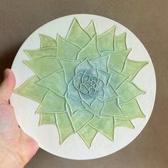 a hand holding a white plate with a green flower on it