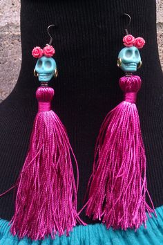 a pair of pink tasselled earrings with skulls and flowers on them, hanging from a black mannequin