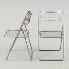 two metal chairs sitting next to each other on a white surface with one chair facing the camera