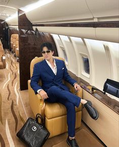 a man in a blue suit and sunglasses sitting on an airplane with his handbag