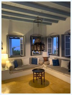 a living room filled with lots of furniture next to two large windows on the wall