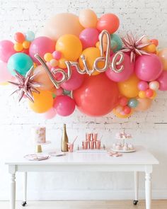 a white table topped with lots of balloons next to a wall filled with stars and the word bride