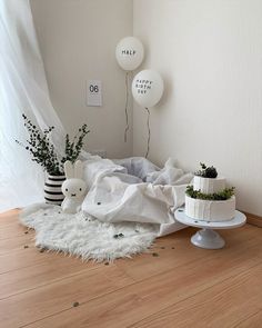 a white cake sitting on top of a wooden floor next to two vases filled with plants