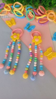 some colorful beads and hair clips on a pink table next to green plants with flowers