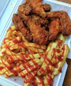 fried chicken and french fries with ketchup drizzled over them on a plastic tray