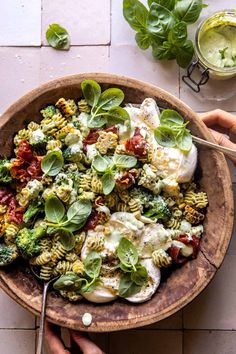 two hands holding a wooden bowl filled with pasta and vegetables