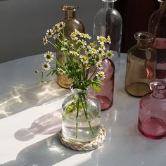 three vases with flowers in them sitting on a table next to other glass bottles