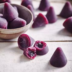 a bowl filled with purple fruit sitting on top of a wooden table next to other pieces of fruit