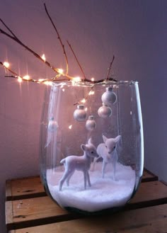 a glass vase filled with snow and small white deer figurines sitting on top of a wooden table