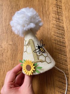 a hand is holding a piece of felt with a bee on it and a sunflower