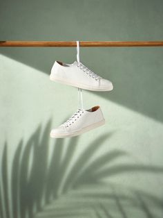 two pairs of white shoes hanging from a wooden rail with shadow on the wall behind them