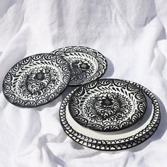 three black and white plates sitting on top of a white cloth covered tablecloth,