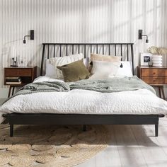 a bed with pillows and blankets on top of it next to two wooden nightstands