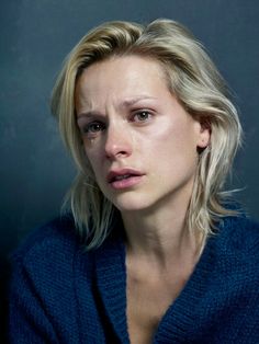 a woman with blonde hair wearing a blue sweater and looking at the camera while posing for a portrait