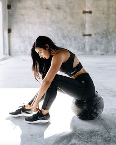 a woman is tying her shoes while sitting on an exercise ball in the middle of a room