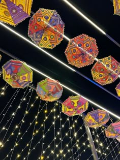 many colorful umbrellas are hanging from the ceiling in front of string lights at night