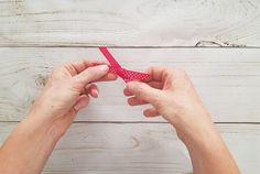 two hands are holding a piece of red paper with white polka dots on it, while another hand is tying the string