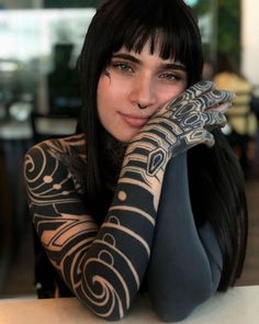 a woman with black hair and tattoos on her arm holding her hand up to her face