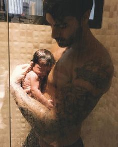 a man holding a baby in his arms while standing next to a glass shower door