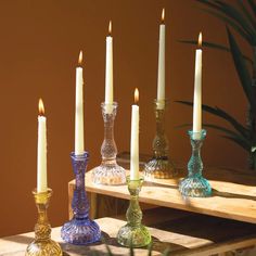 there are many different colored glass candles on the table with one candle in the middle