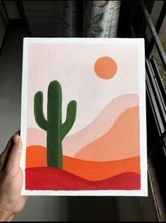 a person holding up a card with a cactus in the desert on it's side