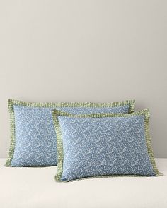 two blue and green pillows sitting on top of a white bed next to each other