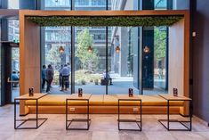 an empty bench in front of a large glass window with people walking by on the sidewalk