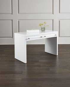 a white desk sitting on top of a hard wood floor next to a vase with flowers