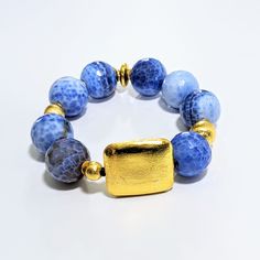 Discover the stunning beauty and unique properties of Ro & Gieo's Blue Fire Agate and 24 Karat Goldplated Brushed Brass Bracelet. Luxurious and eye-catching, this bracelet combines the natural healing energy of blue fire agate with the elegance of 24 karat goldplated brass. Elevate your style and energy with this one-of-a-kind piece. Ro & Gieo Blue Fire Agate & 24 Karat Goldplated Brass Bracelet Bead size - 19 mm 7 inches bracelet length If you want your bracelets in a different size than 7 inch Adjustable Faceted Agate Jewelry, Gold Bracelets With Lapis Lazuli And Natural Stones, Spiritual Sapphire Bracelet Jewelry, Blue Natural Stone Bangle Jewelry, Bohemian Blue Faceted Bracelet, Blue Gemstone Beads Bangle Jewelry, Blue Gemstone Bead Bangle, Blue Gemstone Beads Bangle, Gold Agate Gemstone Bracelets