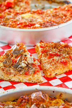 two pizzas sitting on top of a red and white checkered table cloth next to a casserole dish