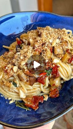 a blue plate topped with pasta covered in sauce and toppings on top of it