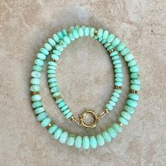 two bracelets with turquoise beads and gold accents on a beige carpeted floor in front of a white wall