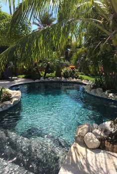 an outdoor swimming pool surrounded by palm trees and rocks with water running down the side