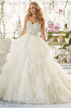 a woman in a wedding dress standing next to a flower filled room with flowers on the walls