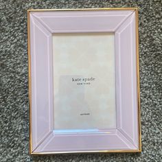 a pink and gold frame with the words kate spade on it, sitting on carpet