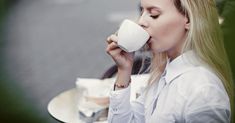 a woman sitting at a table drinking out of a coffee cup with her eyes closed