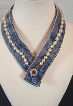 a white mannequin wearing a blue jean necklace with pearls and a button on it