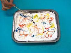 someone using a toothbrush to decorate a cake with white frosting and colorful swirls