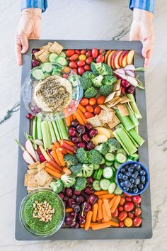 a tray filled with vegetables and dips on top of a marble table next to a person