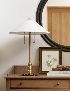 a lamp sitting on top of a wooden dresser next to a framed picture and books