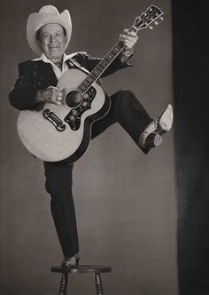 a black and white photo of a man with a guitar on top of a stool