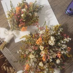 two bouquets of dried flowers on top of a piece of paper next to a cell phone