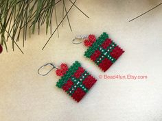 two red and green beaded earrings hanging from a christmas tree ornament on a white surface