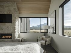 a bedroom with a bed, chair and fireplace in the corner near large windows that look out onto mountains