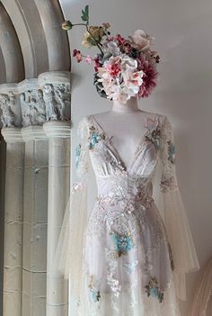 a white dress with flowers on the head and sleeves is displayed in front of a wall