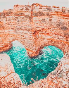 an aerial view of the water and rocks at the ocean's edge, with a rock arch in the foreground