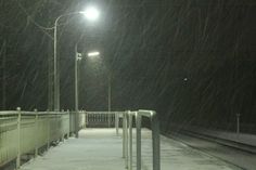 a snow covered walkway next to a street light at night with no one on it