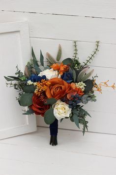 a bridal bouquet with orange, blue and white flowers on a wooden table next to a door