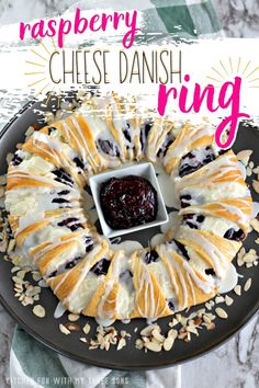 a cheese danish ring with blueberries and almonds on a black plate next to a jar of jam